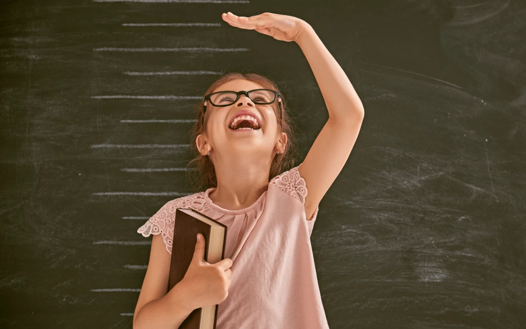 Happy Little Girl Holding A Book And Happily Measuring Her Height