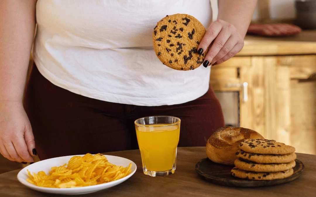 a-fat-lady-holding-a-chocolate-cookie-with-table-full-of-cookies-snacks-juices